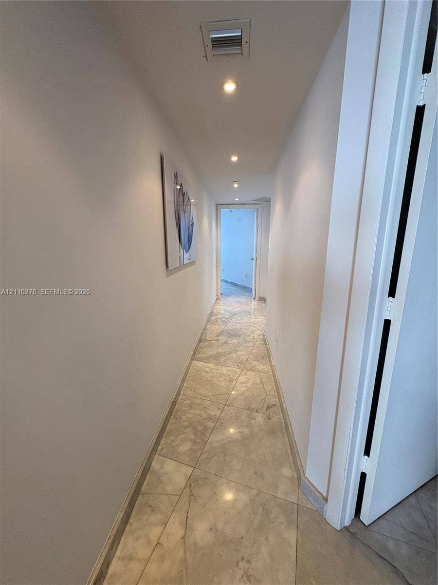 Hallway featuring large-format polished stone tile flooring and recessed ceiling lighting