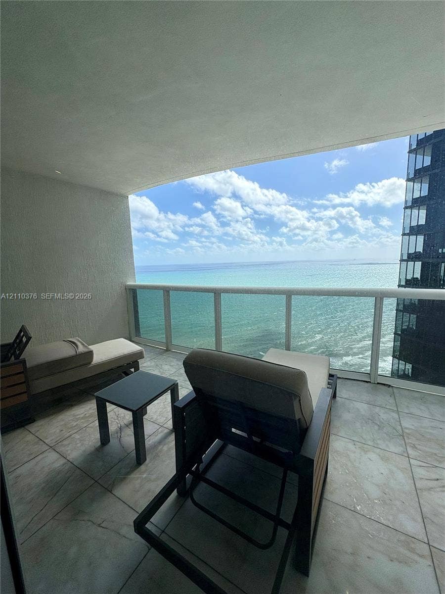 Covered balcony featuring large-format tile flooring and a glass panel railing
