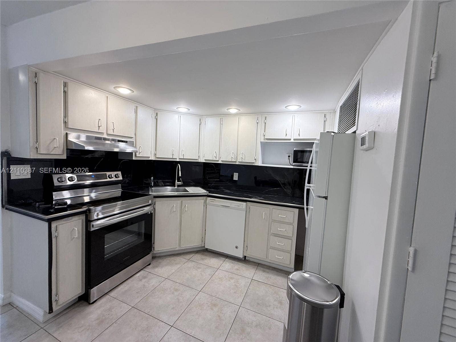Kitchen featuring white cabinetry, black stone-finish countertops, stainless steel appliances, recessed lighting, and tile flooring