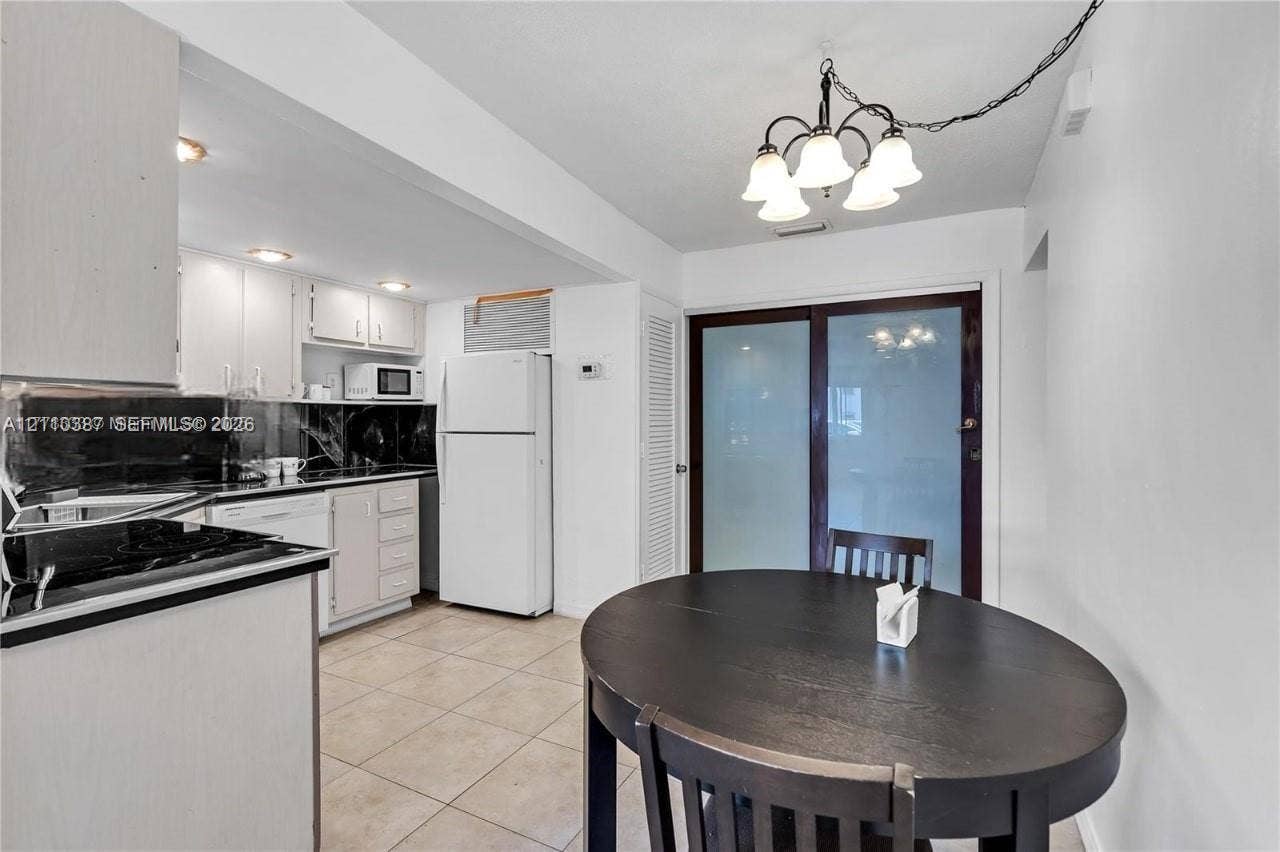 Kitchen featuring flat-panel cabinetry, dark stone-finish countertops, tile flooring, five-light chandelier, and glass-paneled sliding door