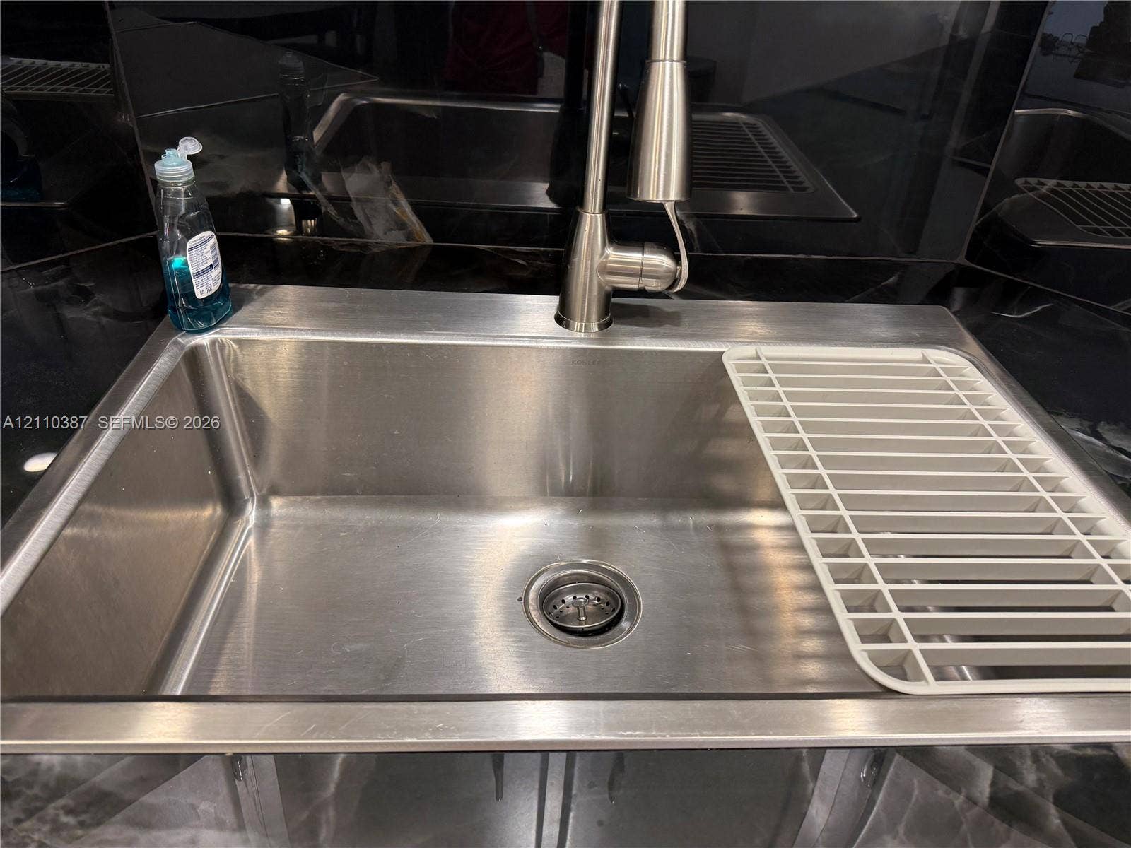Undermount stainless steel kitchen sink featuring a high-arc pull-down faucet and dark stone-surface countertops