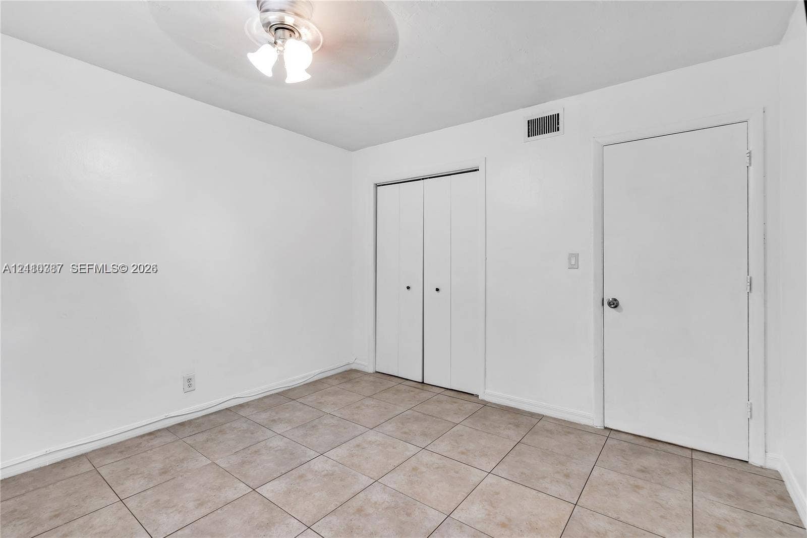 Neutral-toned tile flooring, white interior walls, ceiling-mounted light fixture, and closet with bifold doors