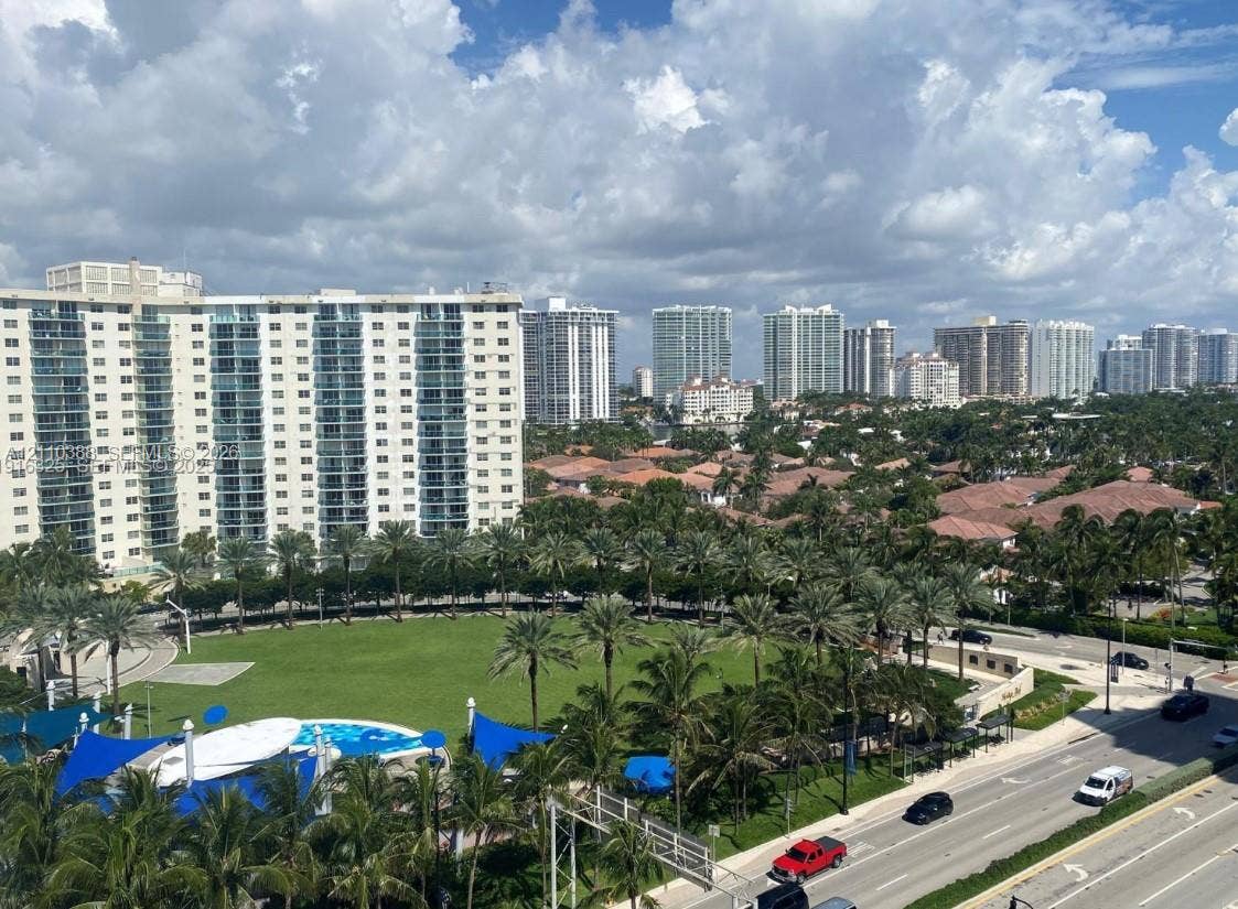 High-rise urban landscape featuring expansive green space, mature palm trees, multi-story residential structures, and blue shade structures