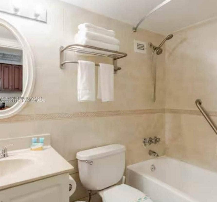 Bathroom featuring floor-to-ceiling tile, oval wall mirror, integrated vanity countertop with sink, and a combination tub and shower with metallic hardware