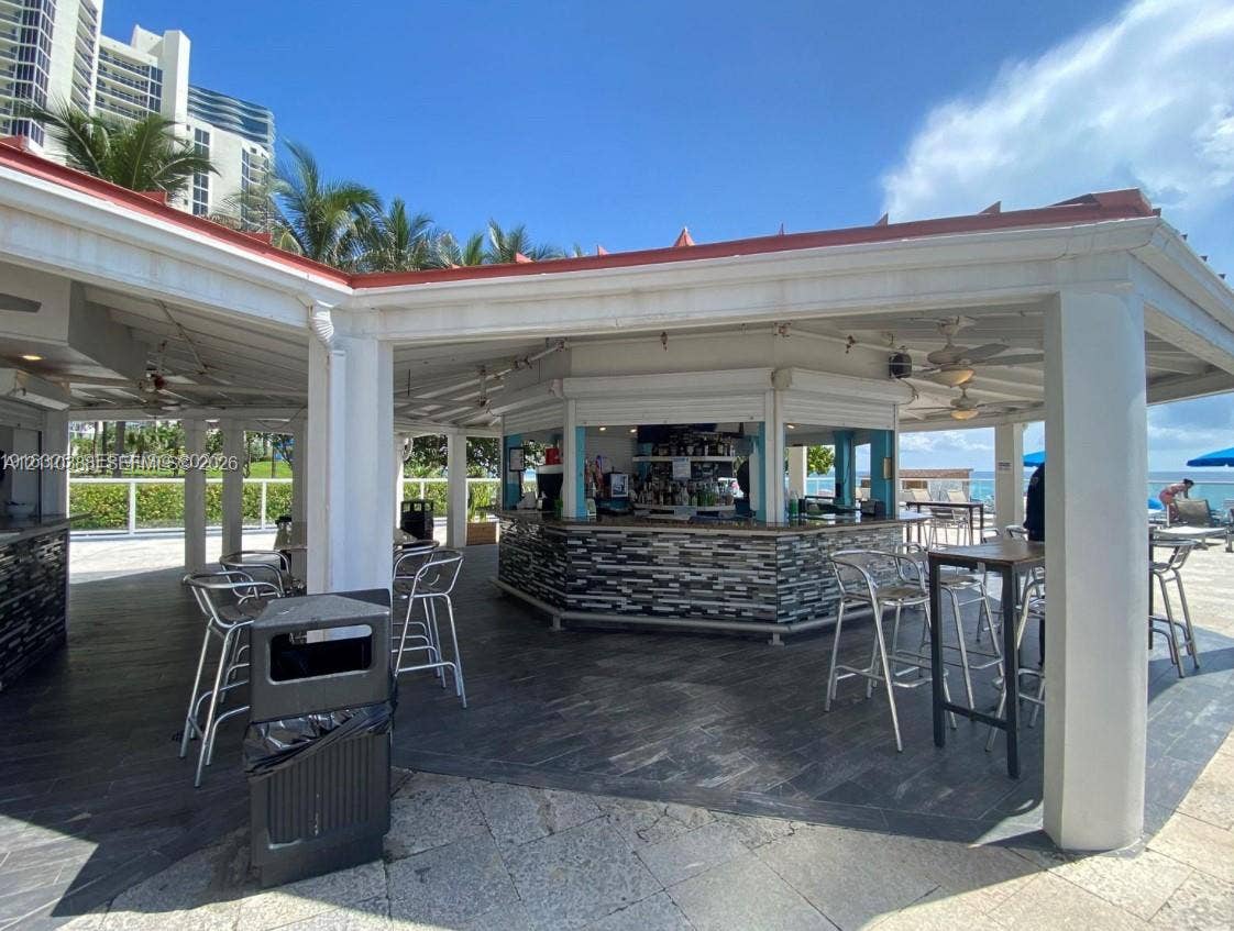 Covered outdoor bar featuring a stacked-stone facade, slate-tile flooring, ceiling fans, and structural columns