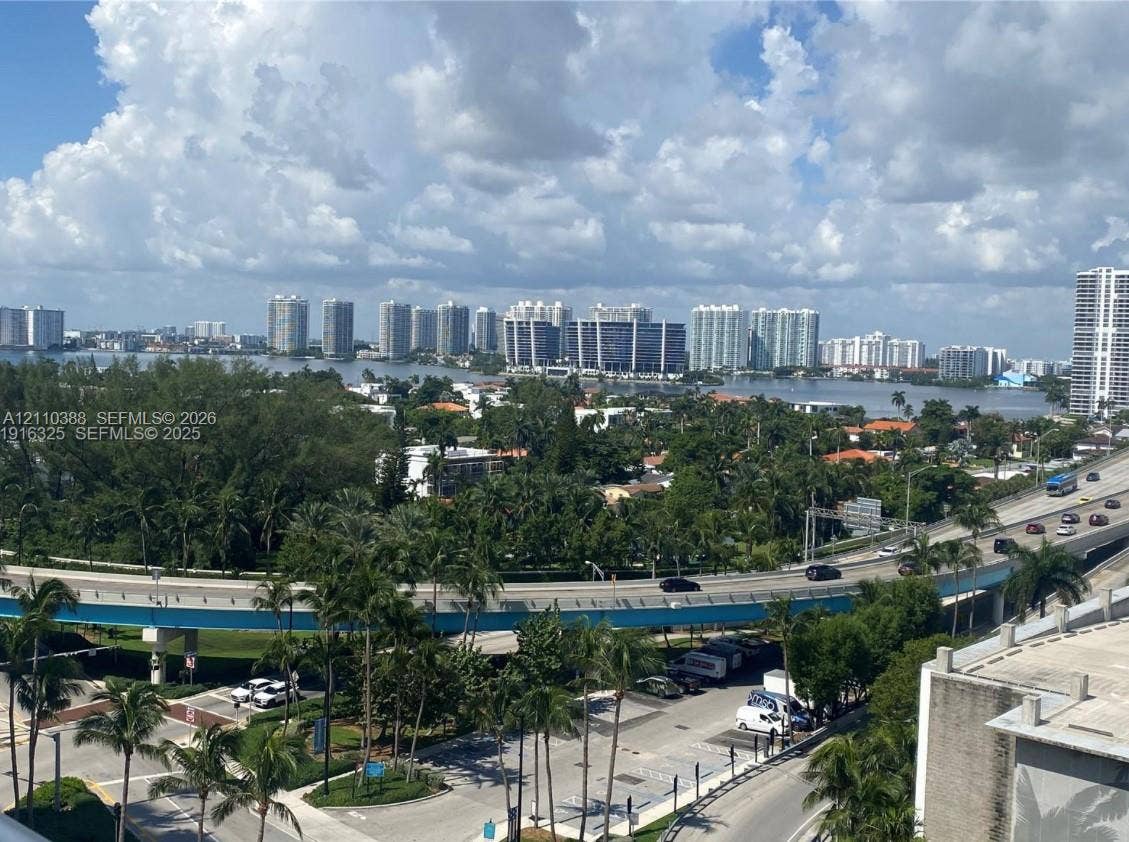 Panoramic cityscape featuring coastal waterway, high-rise buildings, and mature palm trees