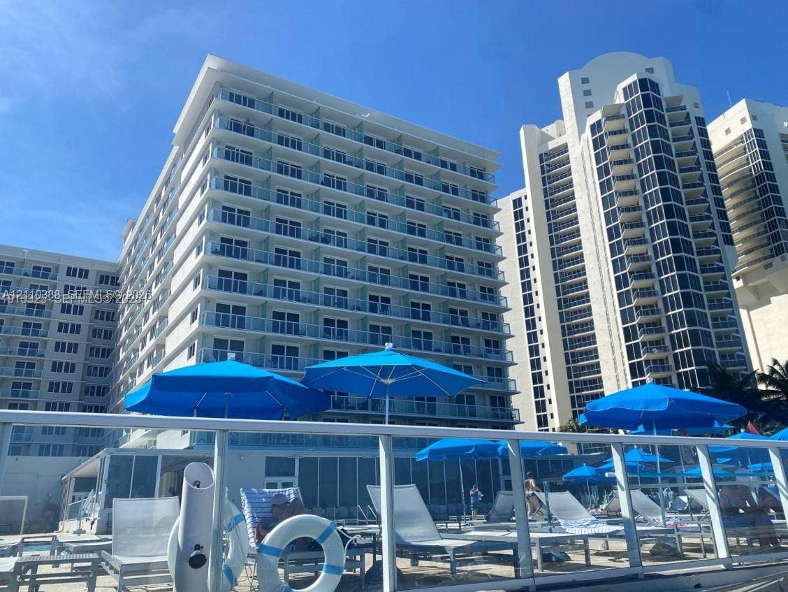 High-rise residential exterior featuring expansive glass-railed balconies, a multi-story concrete facade, and a ground-level swimming pool deck