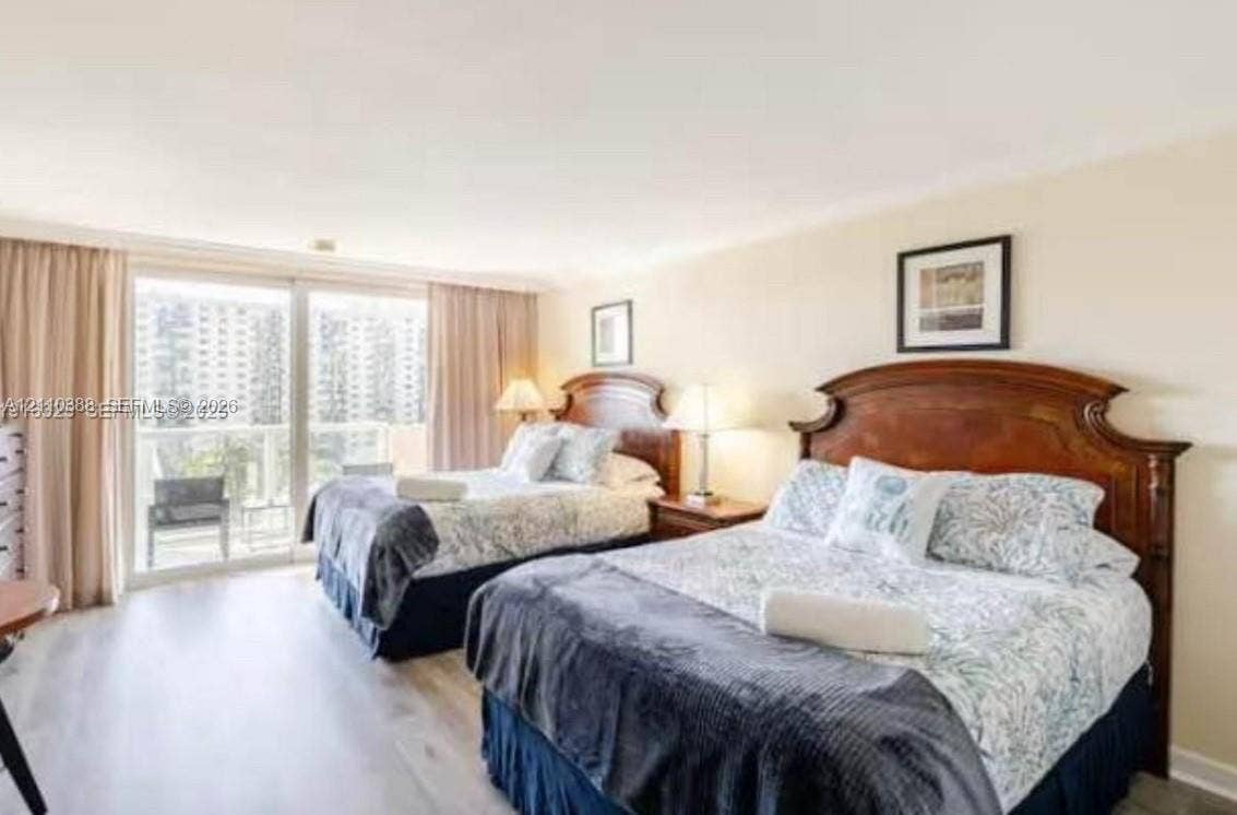 Neutral-toned bedroom featuring wood-finish flooring, floor-to-ceiling drapery, and sliding glass doors providing outdoor access
