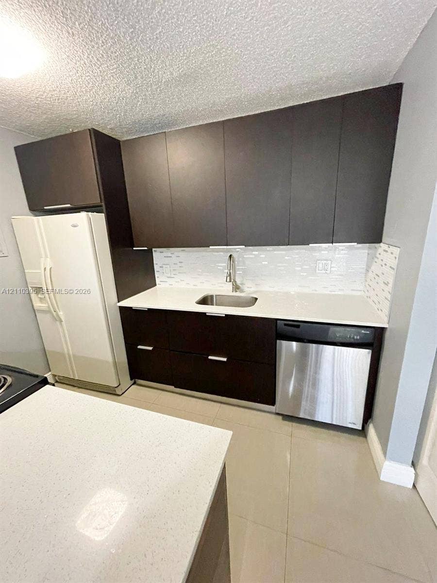 Dark-toned cabinetry featuring flat-panel doors, quartz countertops, stainless steel undermount sink with arched faucet, mosaic tile backsplash, and stainless steel dishwasher