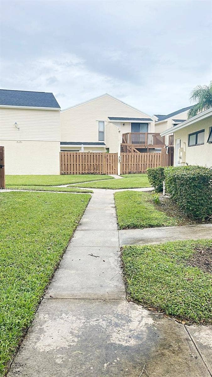 Exterior area featuring a paved walkway, manicured lawn, wood privacy fencing, and second-story wood balcony
