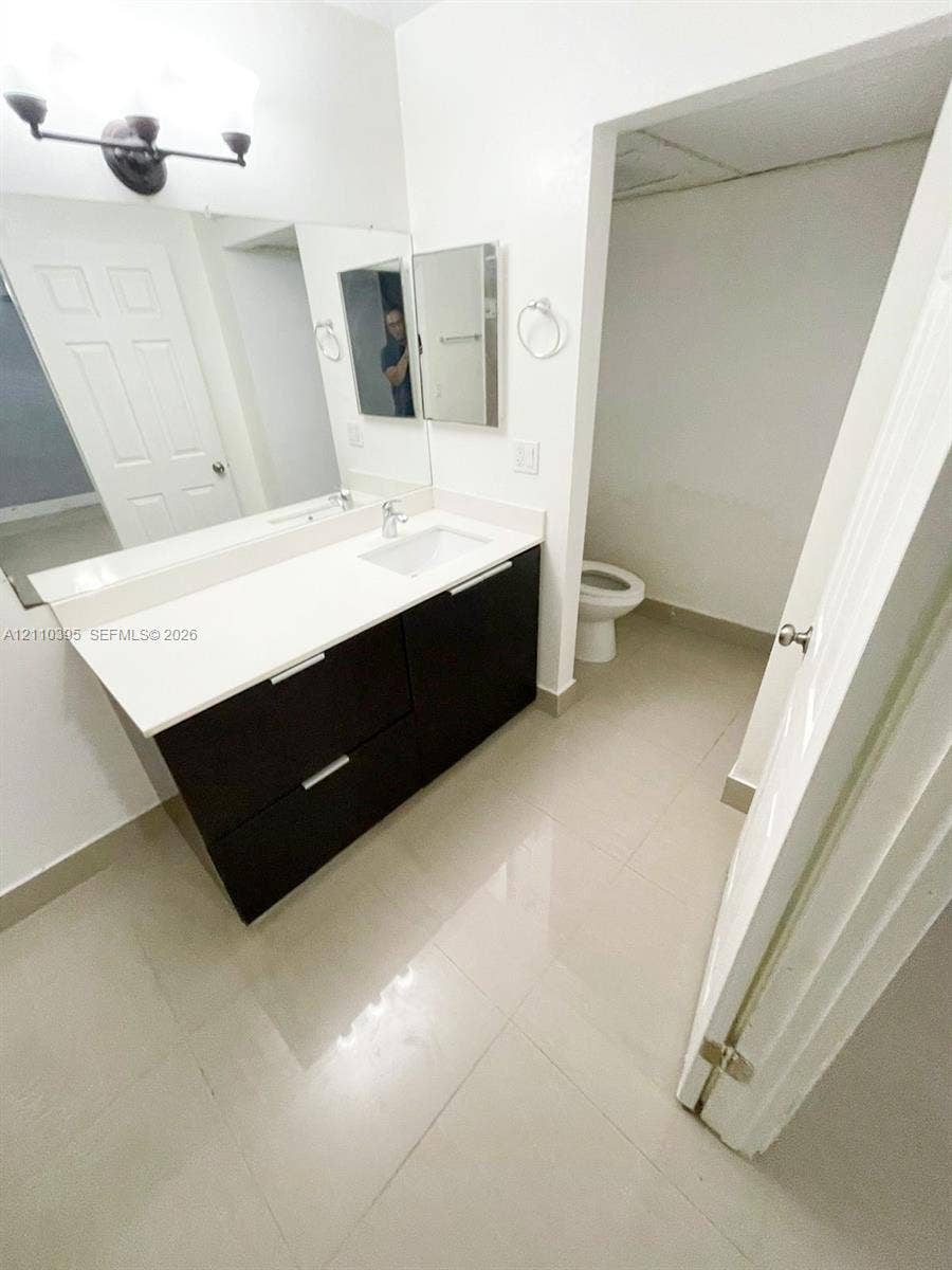 Floating vanity featuring a dark-toned cabinet, integrated countertop with a rectangular basin, large wall-mounted mirror, three-light fixture, and ceramic tile flooring