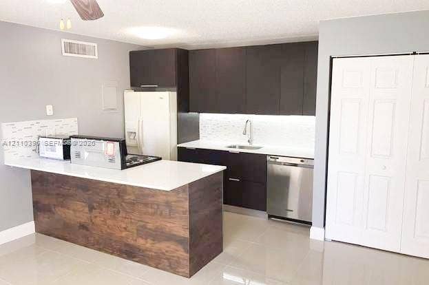 Kitchen featuring dark cabinetry, white countertops, stainless steel dishwasher, tile backsplash, and wood-finish breakfast bar
