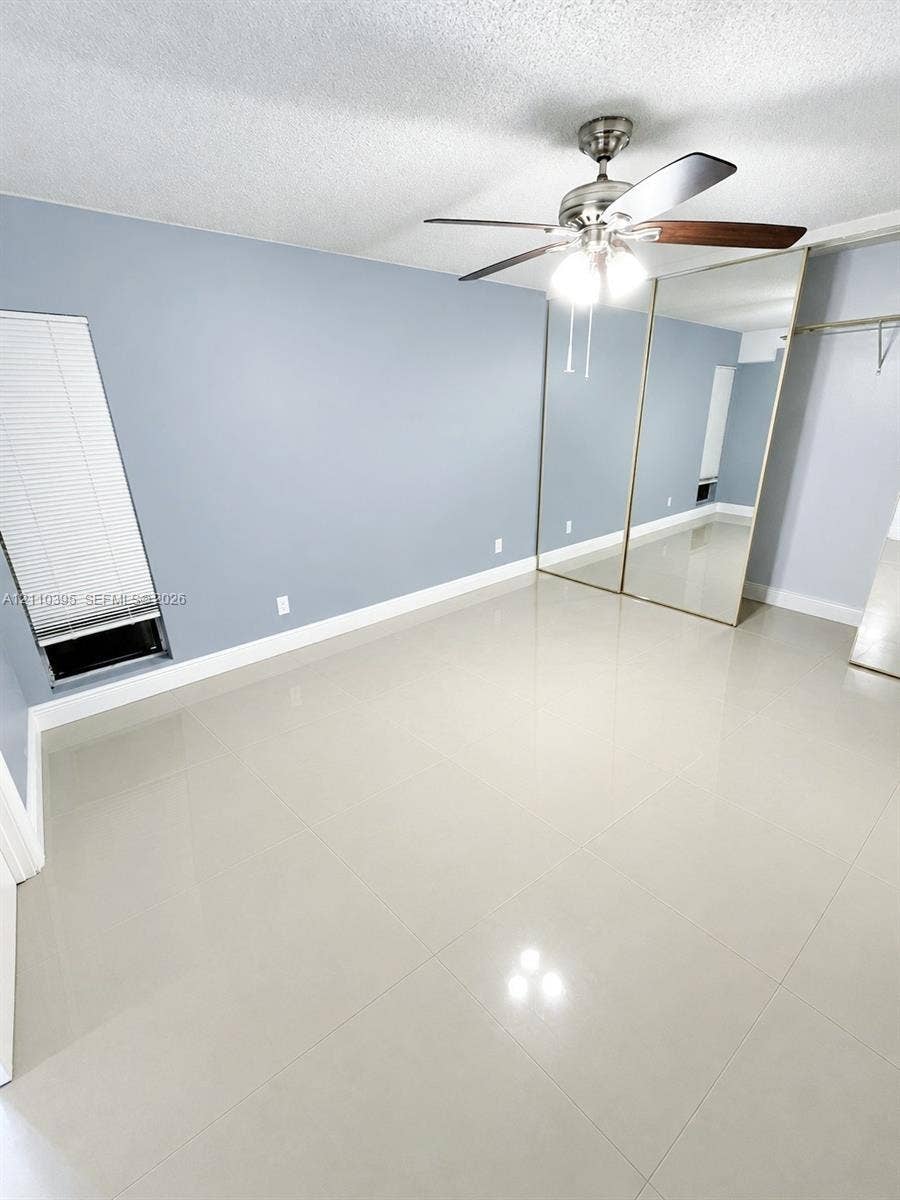 Room featuring large-format tile flooring, mirrored closet doors, a ceiling fan with integrated light fixture, and a window with horizontal blinds