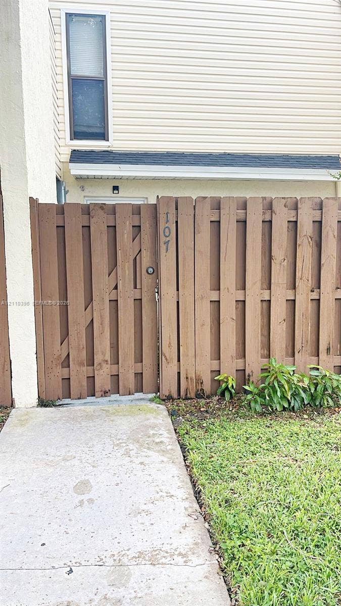 Exterior entrance featuring a private wooden privacy fence, a gated entry, a concrete walkway, and beige horizontal siding