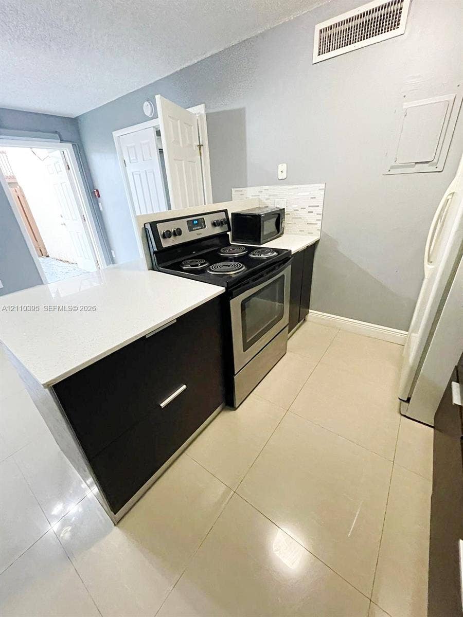 Kitchen featuring dark cabinetry, solid-surface countertops, tile backsplash, stainless steel range, and large-format tile flooring