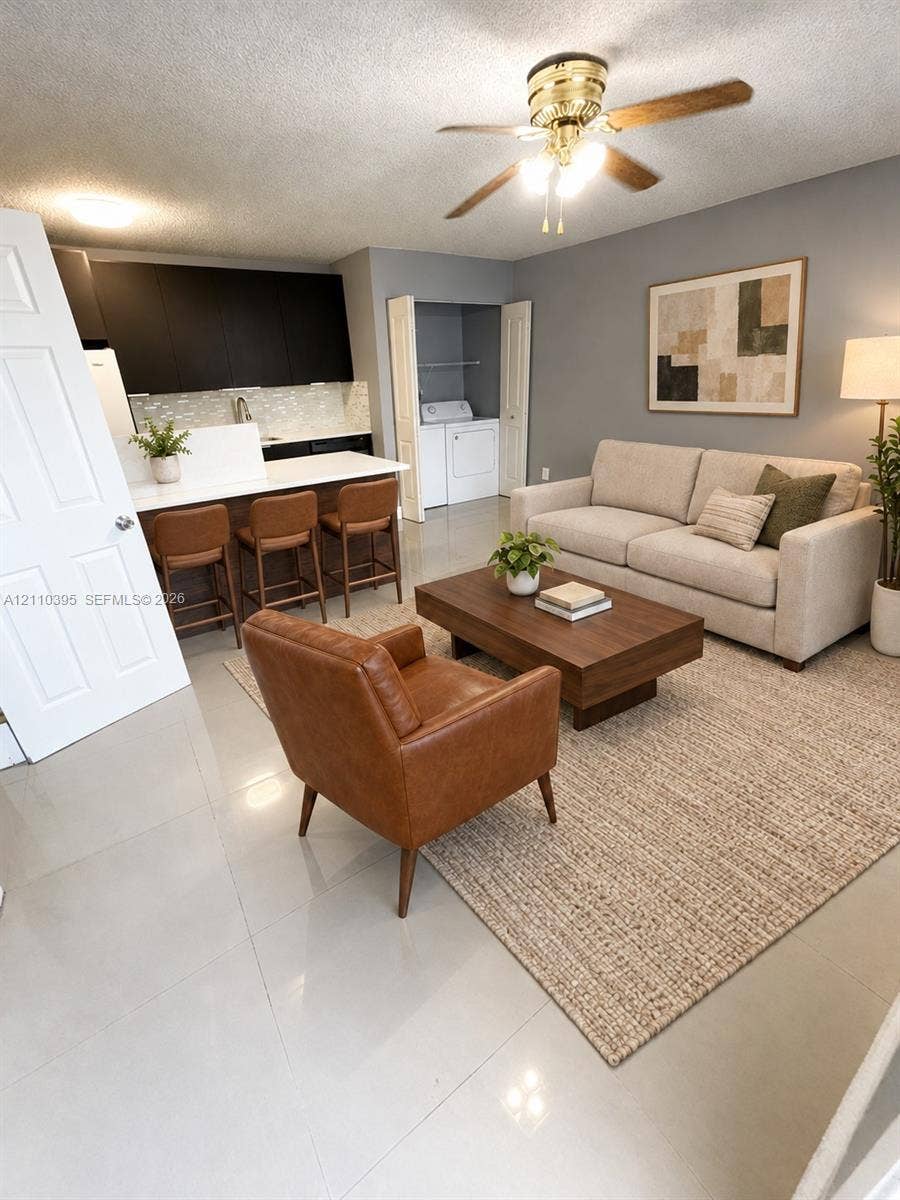 Open-concept living space featuring high-gloss, dark-toned cabinetry, quartz countertops, tile flooring, and an integrated laundry closet with bifold doors