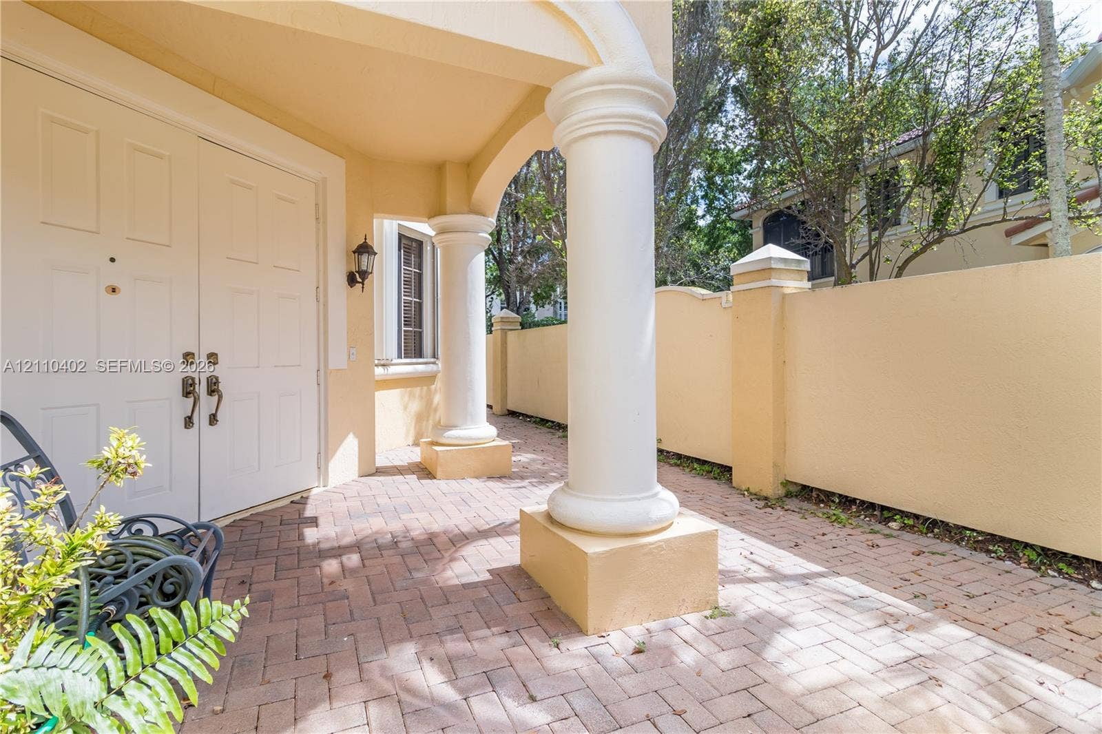 Covered entrance featuring brick-paver flooring, classical architectural columns, and double-door entry