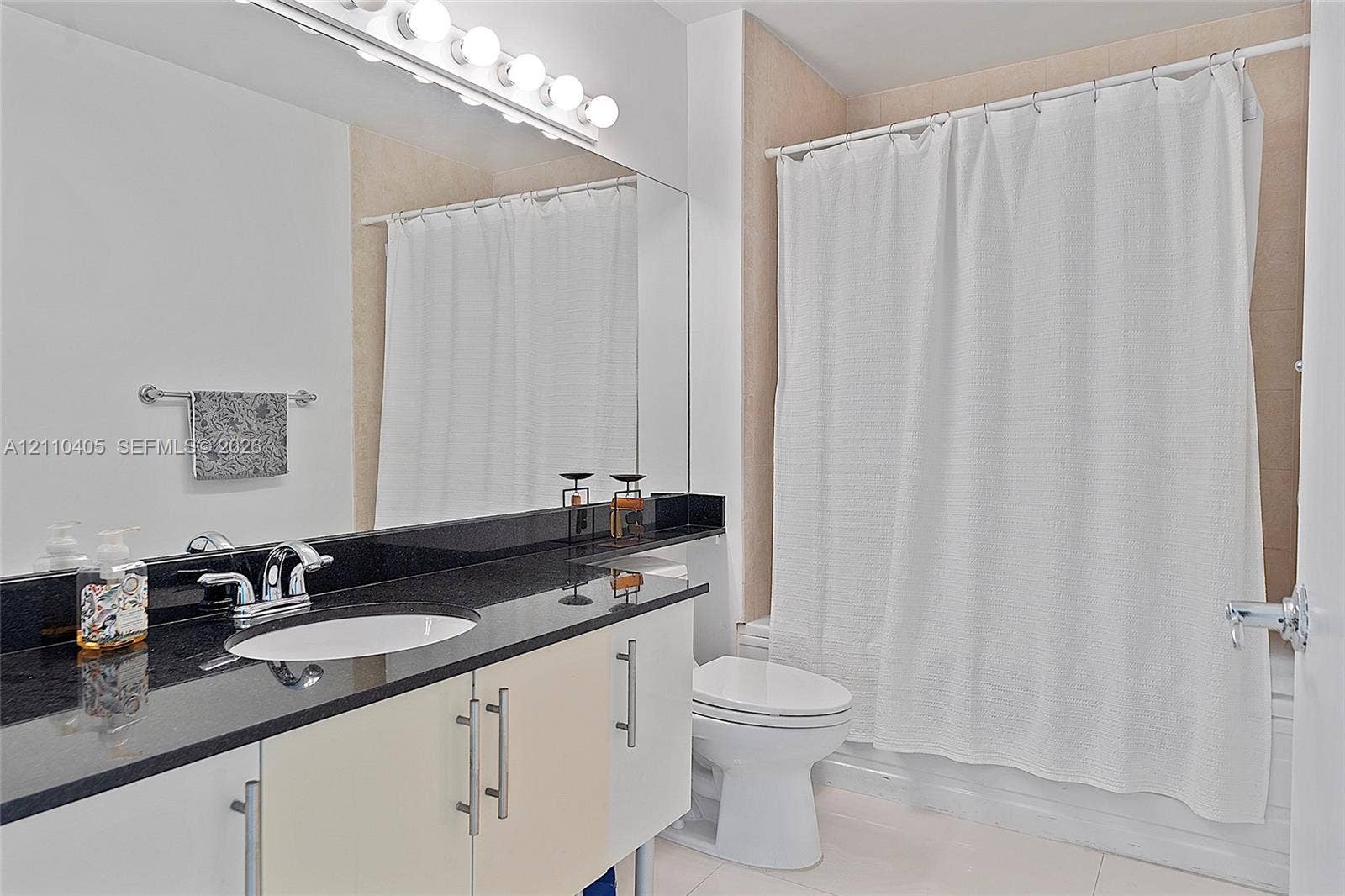Bathroom featuring a white vanity with a black countertop, an undermount oval sink, chrome dual-handle faucet, large wall-mounted mirror, and a multi-bulb light fixture