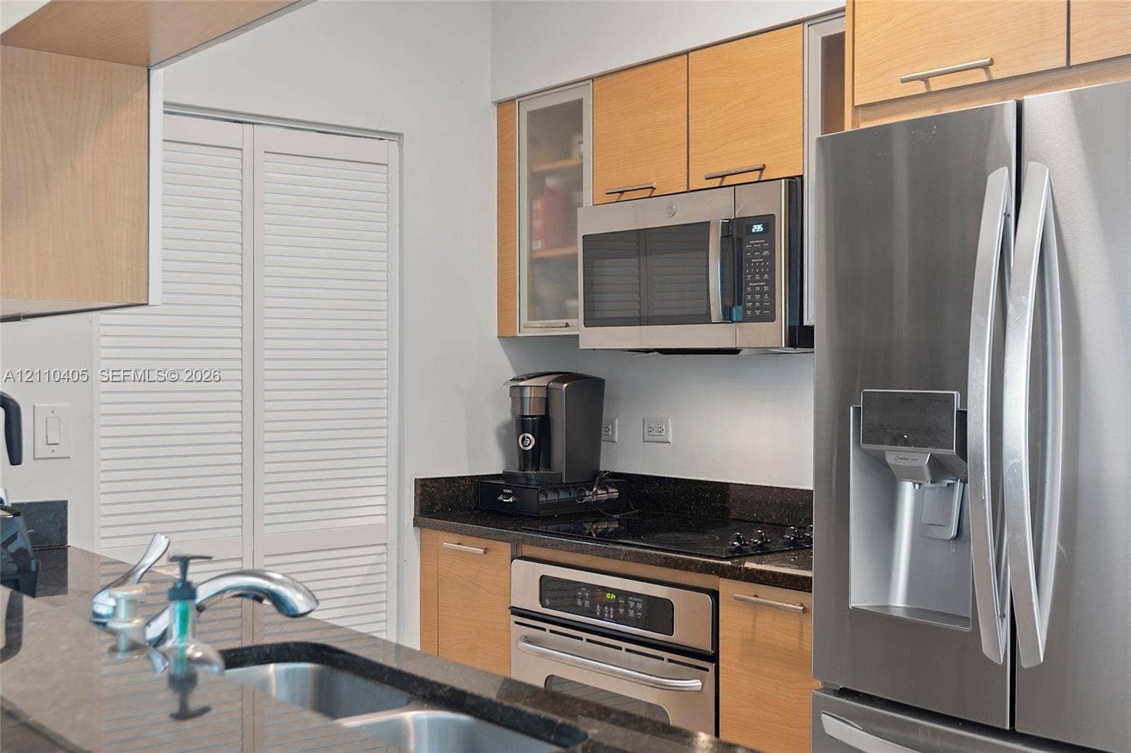 Kitchen featuring light wood-finish cabinetry, dark solid-surface countertops, stainless steel appliances, and a double-basin undermount sink