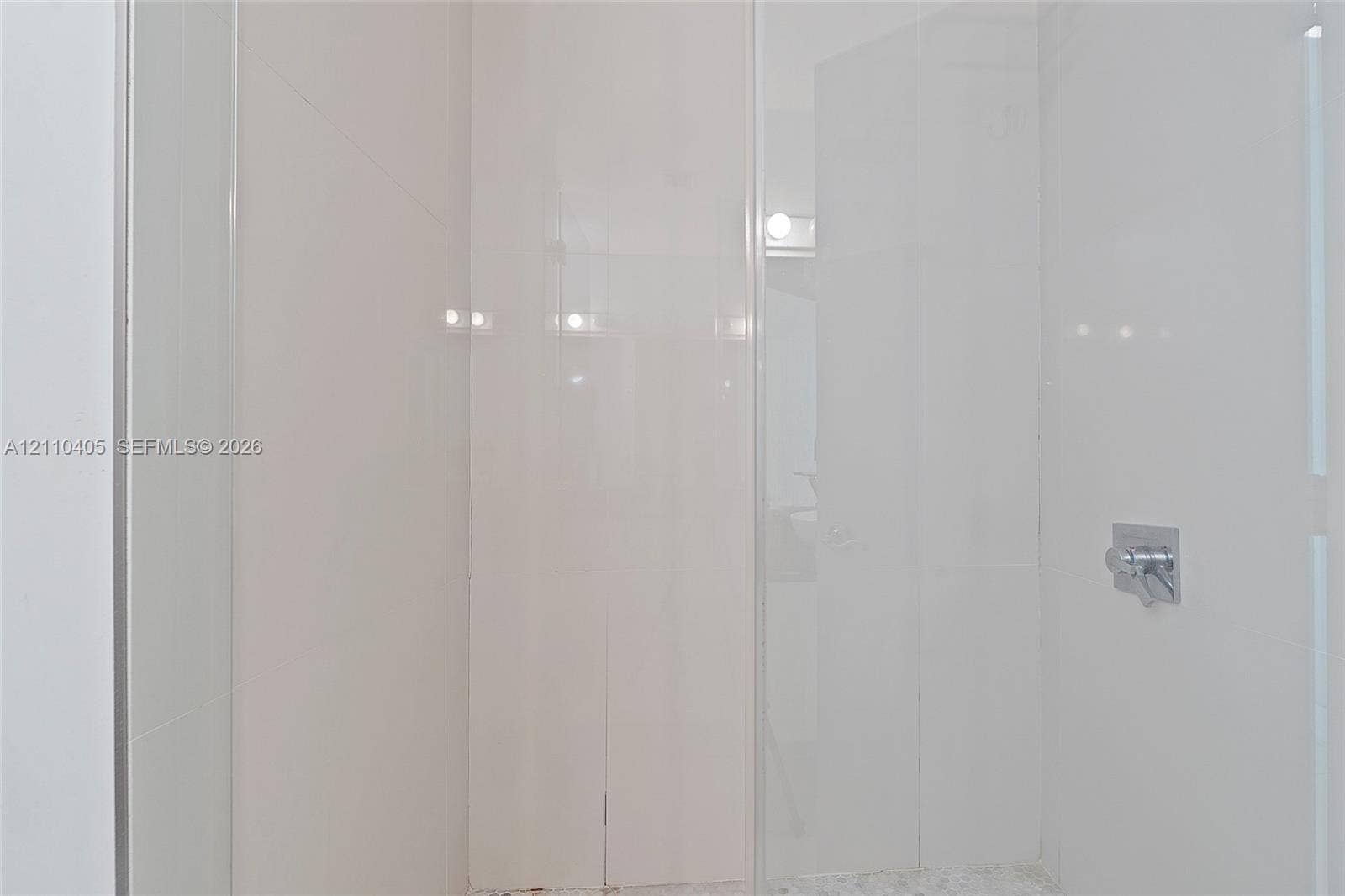 Walk-in shower enclosure with full-height white tile wall surround, glass door, and polished chrome fixtures