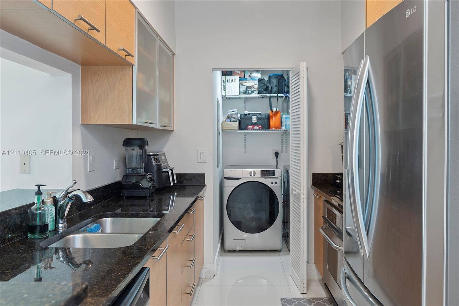 Kitchen featuring wood-finish cabinetry, dark stone countertops, stainless steel appliances, and a laundry closet with shelving