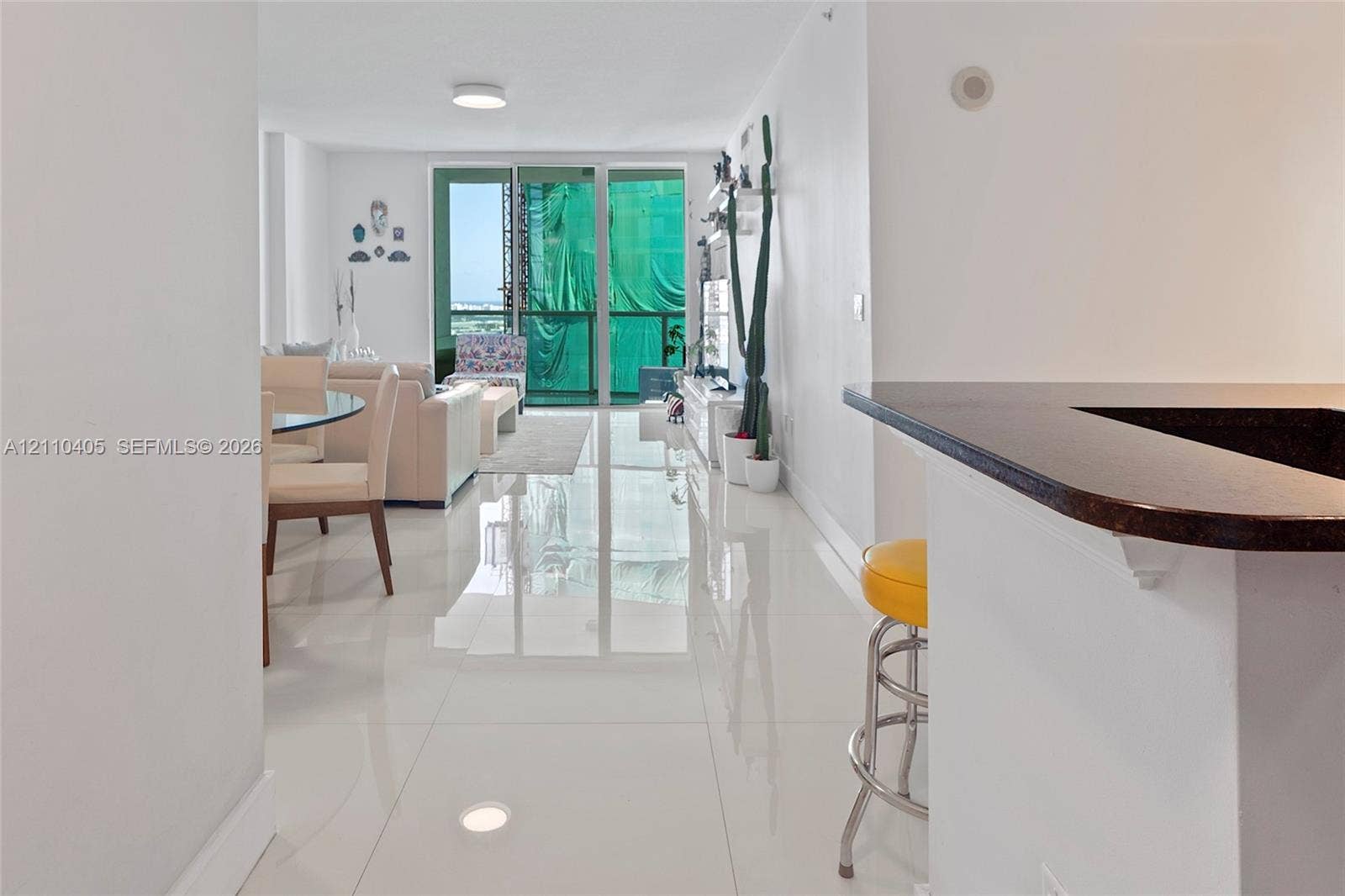 Open-concept interior featuring large-format polished tile flooring, a kitchen breakfast bar with a dark stone countertop, and floor-to-ceiling glass sliding doors