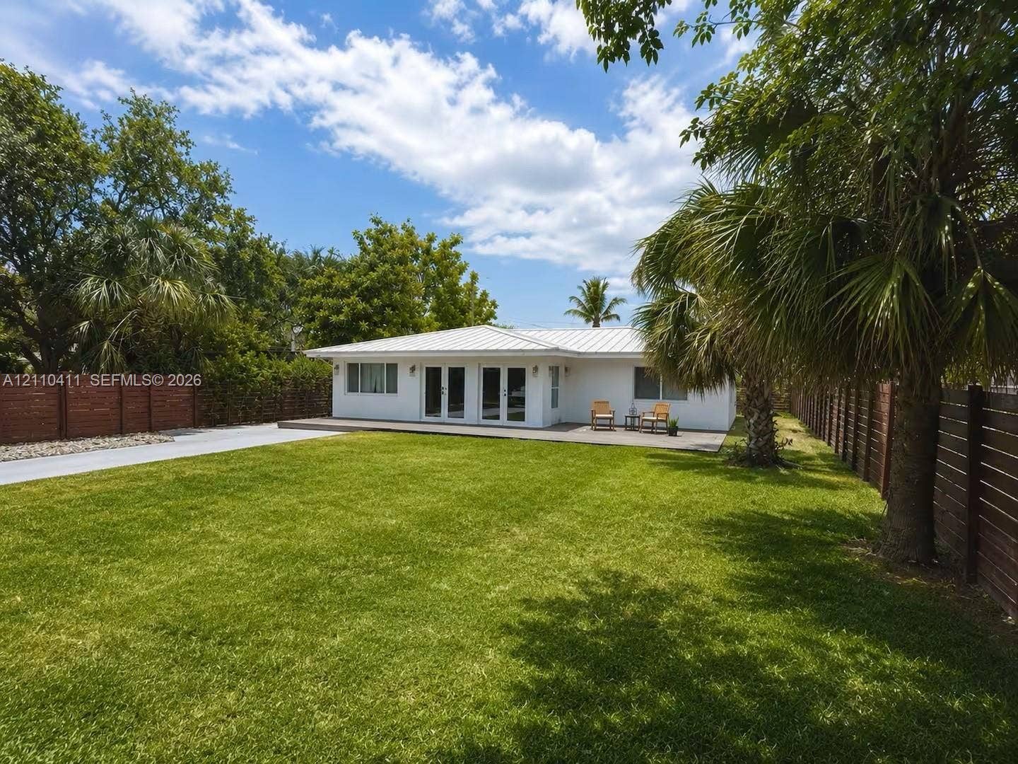 Single-story residence featuring a metal roof, white exterior, multi-panel glass doors, wood-slat fencing, and a spacious lawn