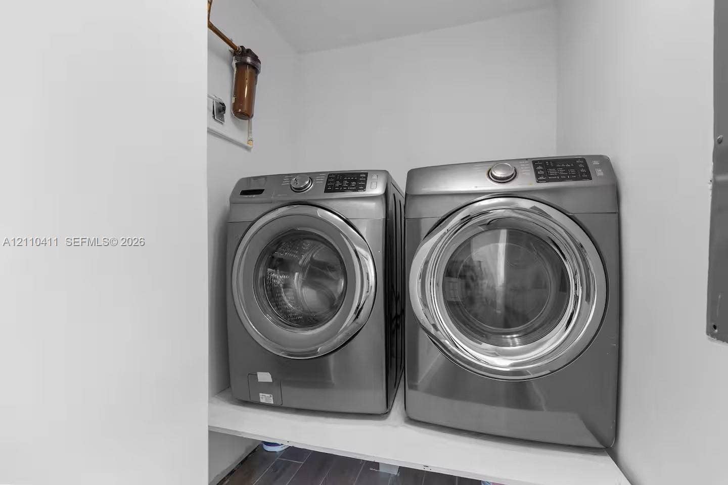 Dedicated laundry alcove featuring stainless steel front-load appliances, built-in shelving, and tile flooring
