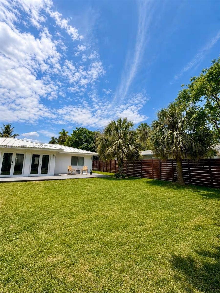 Private backyard featuring a manicured lawn, horizontal wood-slat privacy fencing, mature palm trees, and a concrete patio