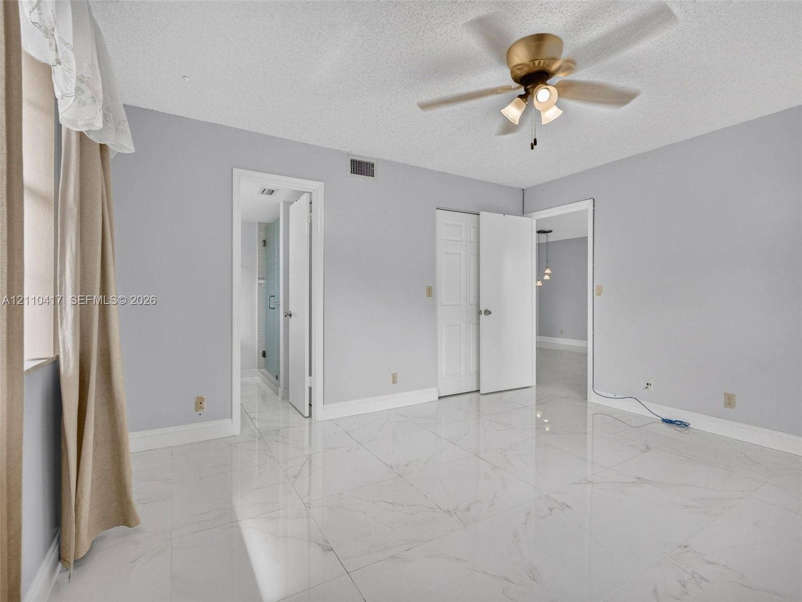 2369 NW 89th Drive, #514, Coral Springs, FL 33065 Polished large-format tile flooring with marble-style veining, accented by a brass-finish ceiling fan with integrated lighting and multi-panel doors