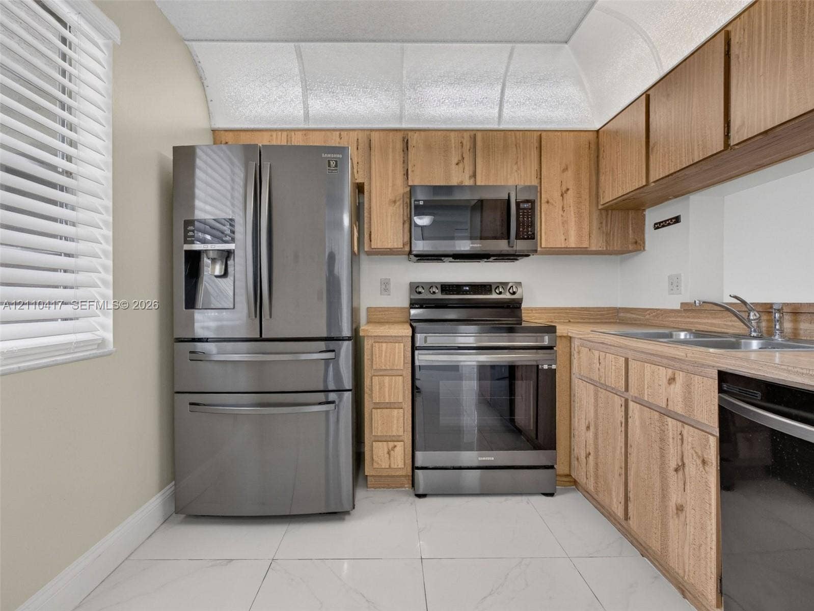 2369 NW 89th Drive, #514, Coral Springs, FL 33065 Kitchen featuring wood-finish cabinetry, stainless steel appliances, a double-basin stainless steel sink, and light-toned tile flooring