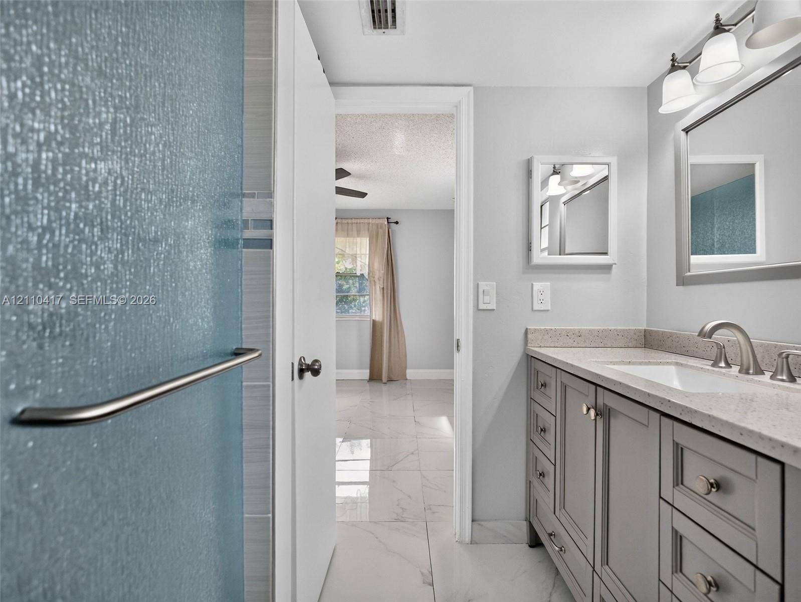 2369 NW 89th Drive, #514, Coral Springs, FL 33065 Bathroom featuring a light-toned vanity with stone-surface countertop, rectangular undermount sink, three-light wall fixture, and marble-finish flooring