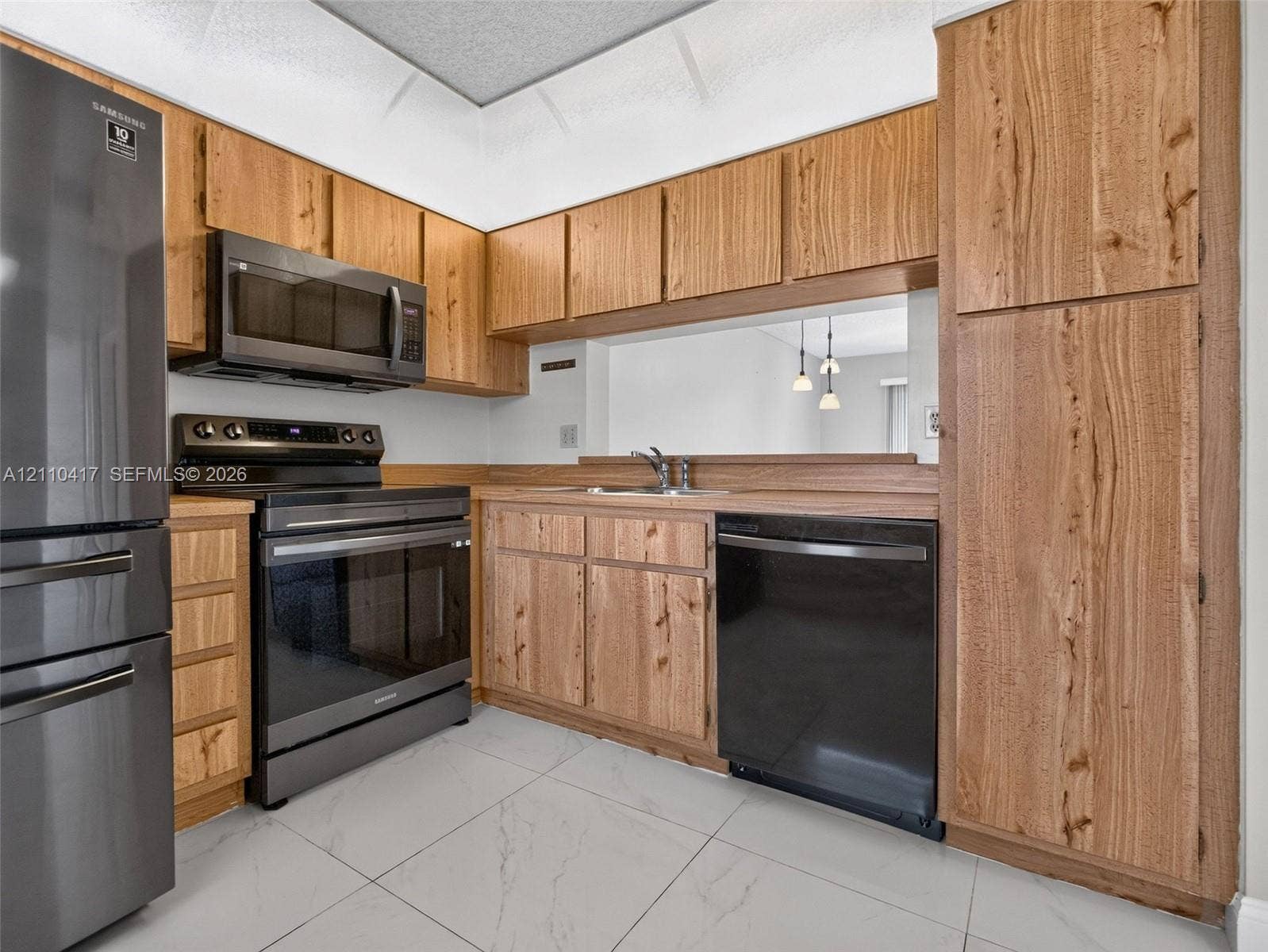 2369 NW 89th Drive, #514, Coral Springs, FL 33065 Kitchen featuring wood cabinetry, stainless steel appliances, a pass-through opening, and large-format tile flooring