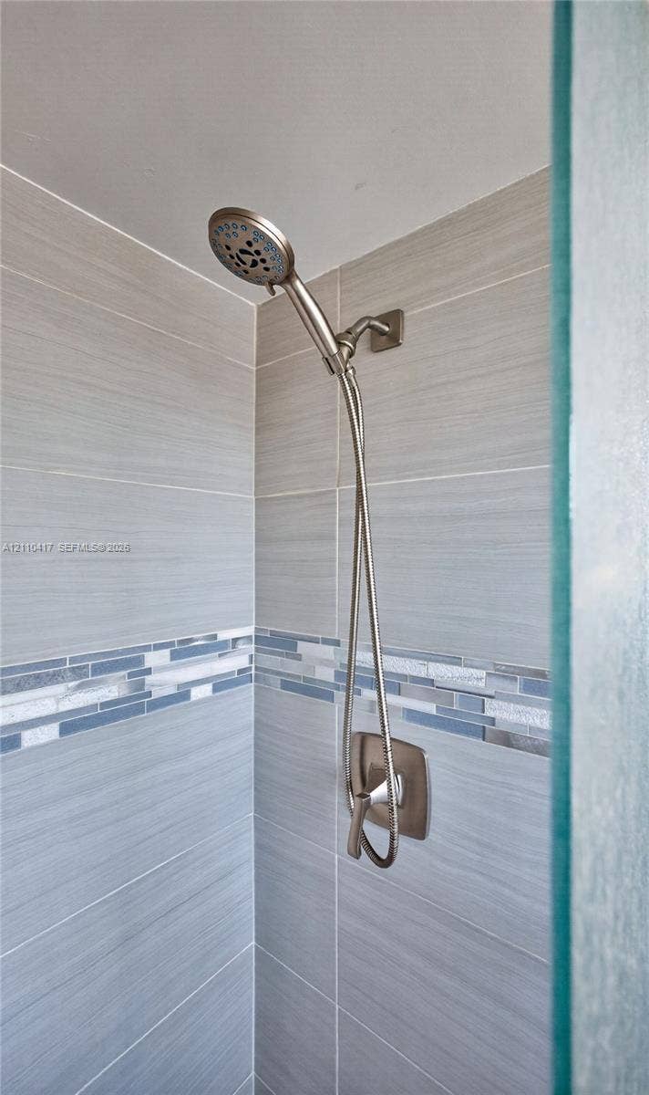2369 NW 89th Drive, #514, Coral Springs, FL 33065 Shower enclosure featuring brushed nickel handheld showerhead, single-handle pressure balance valve, horizontal neutral-toned wall tile, and decorative glass mosaic accent border