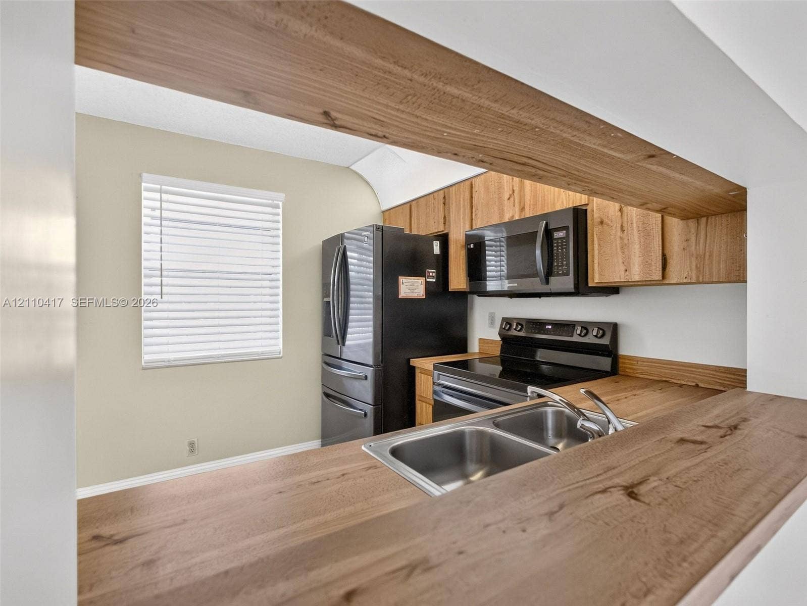 2369 NW 89th Drive, #514, Coral Springs, FL 33065 Kitchen featuring wood-finish countertops, natural wood cabinetry, stainless steel dual-basin sink, and black appliances including a built-in microwave