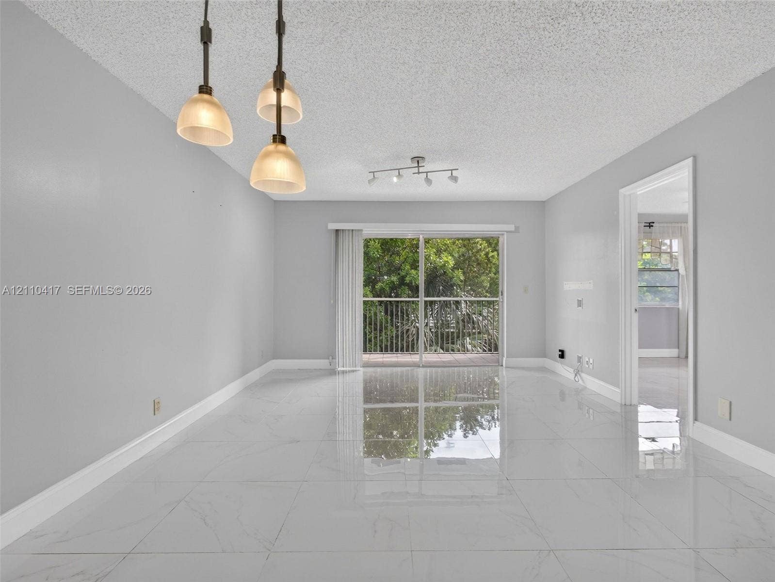 2369 NW 89th Drive, #514, Coral Springs, FL 33065 Large-format polished porcelain tile flooring, sliding glass door with balcony access, triple-pendant light fixture, and multi-directional track lighting