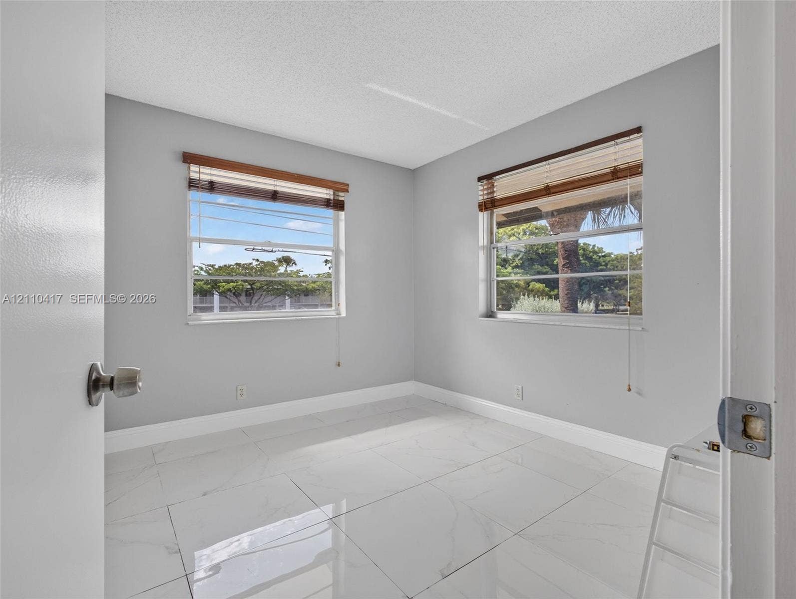 2369 NW 89th Drive, #514, Coral Springs, FL 33065 Neutral-toned interior featuring large-format tile flooring, textured ceilings, and dual windows with built-in horizontal blinds