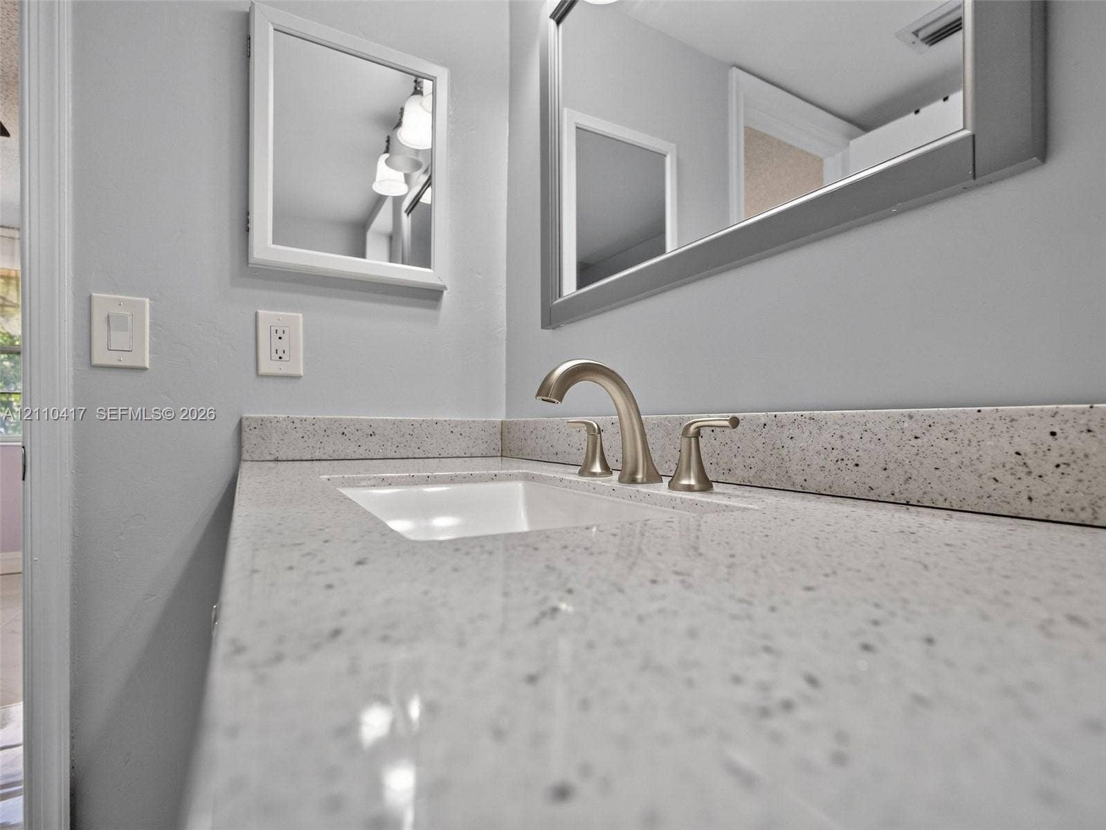 2369 NW 89th Drive, #514, Coral Springs, FL 33065 Vanity featuring a speckled stone-composite countertop, integrated rectangular undermount sink, three-piece arched faucet, large wall-mounted mirror, and medicine cabinet