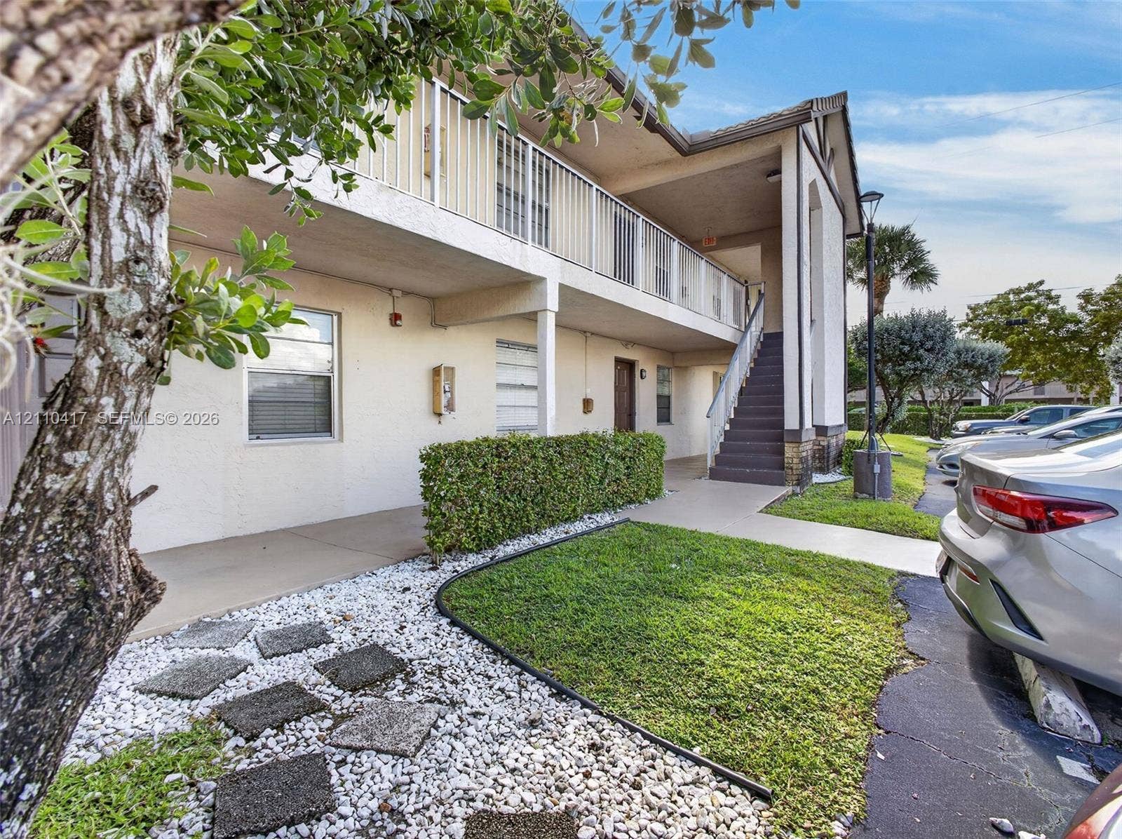 2369 NW 89th Drive, #514, Coral Springs, FL 33065 Multi-story building exterior featuring a covered balcony with metal railings, external staircase, stucco facade, and landscaped grounds with decorative stone paths