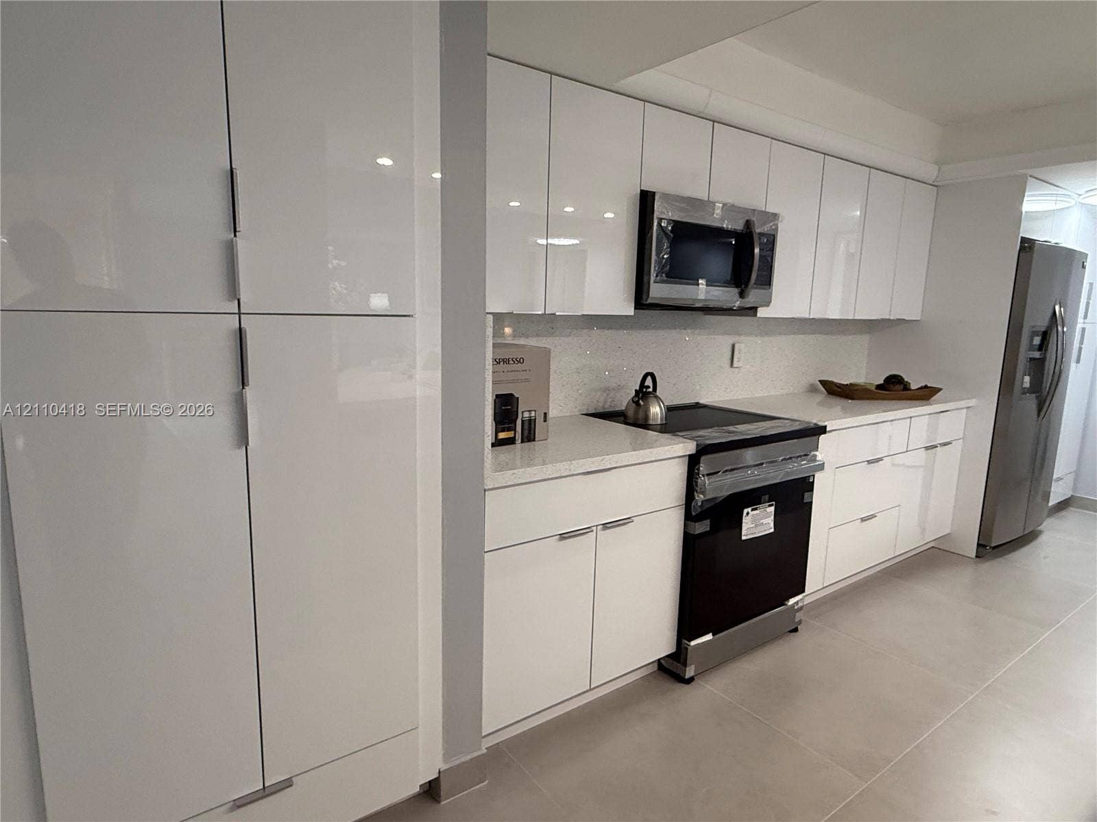 950 Egret Circle, #5409, Delray Beach, Delray Beach, FL 33444 Kitchen featuring high-gloss white cabinetry, quartz countertops, tile backsplash, built-in stainless steel microwave, and large-format floor tile