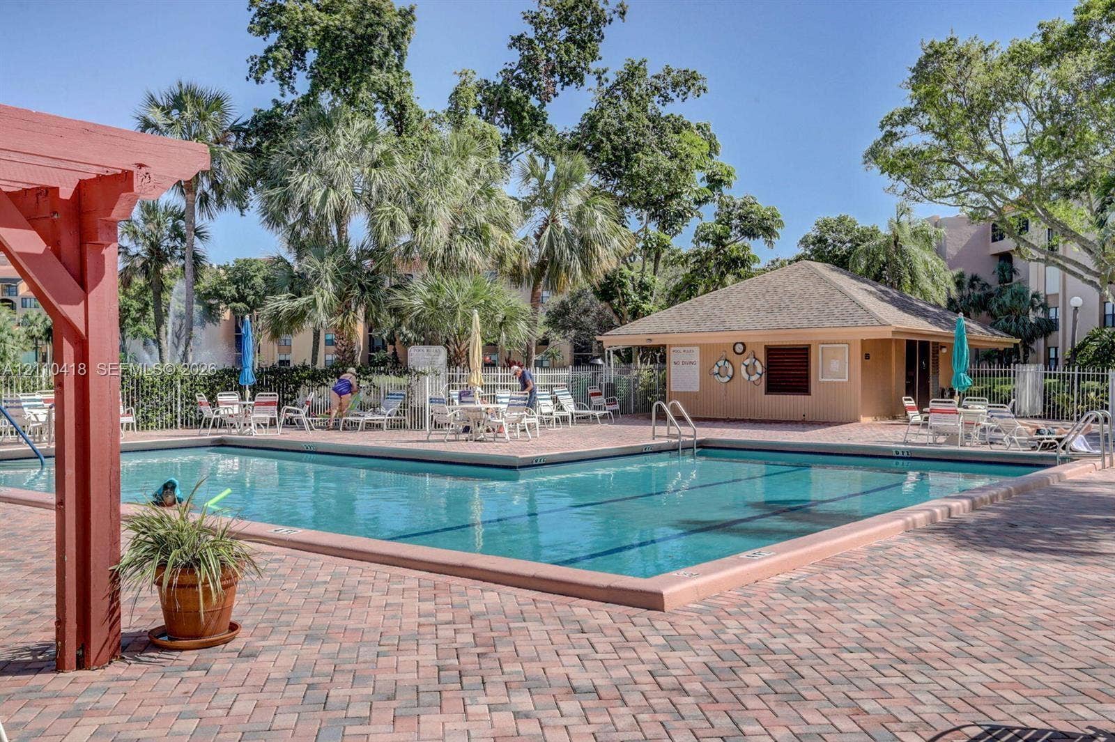 950 Egret Circle, #5409, Delray Beach, Delray Beach, FL 33444 Swimming pool with a brick-paver deck, pergola structure, and poolside cabana surrounded by mature palm trees