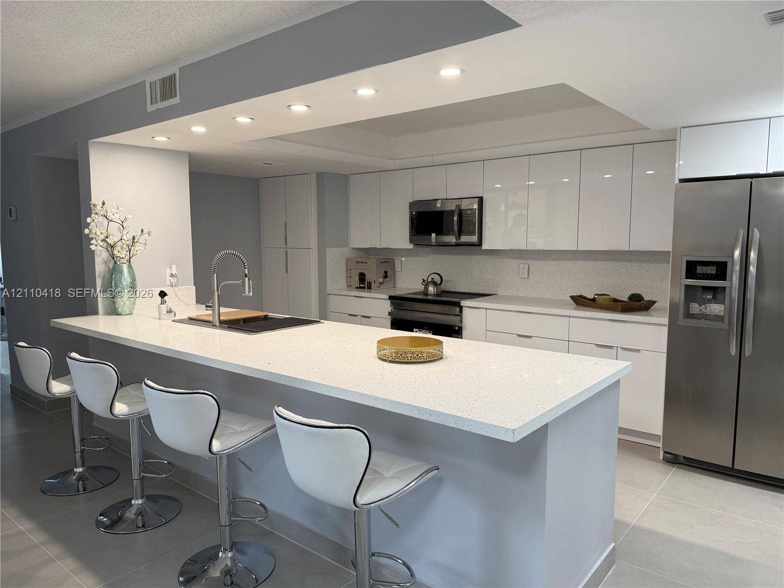950 Egret Circle, #5409, Delray Beach, Delray Beach, FL 33444 Kitchen featuring a large waterfall-edge island, high-gloss white cabinetry, solid-surface countertops, recessed ceiling lighting, and stainless steel appliances
