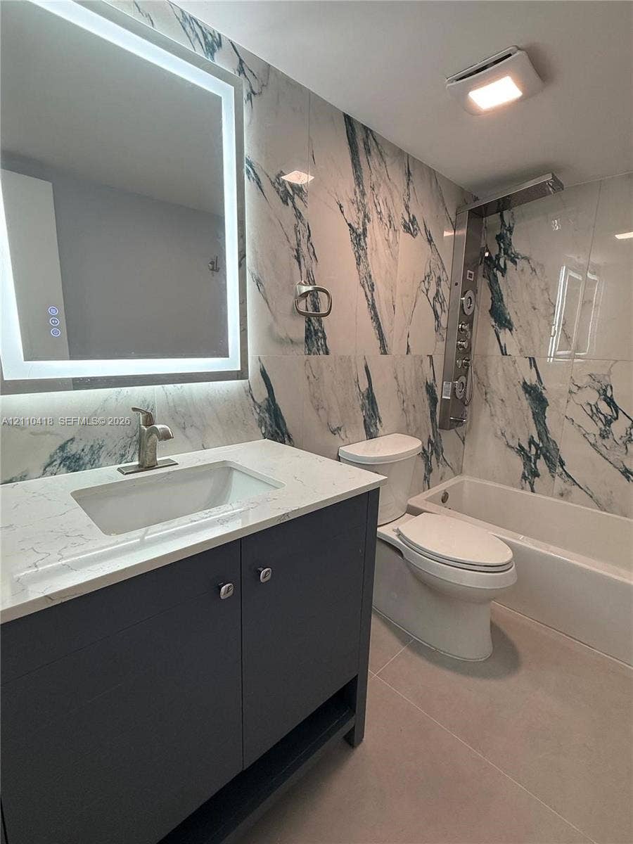 950 Egret Circle, #5409, Delray Beach, Delray Beach, FL 33444 Full-bathroom featuring a dark finish vanity with a rectangular sink, quartz-surfaced countertop, LED-backlit mirror, large-format patterned wall tile, and a multi-head shower panel system