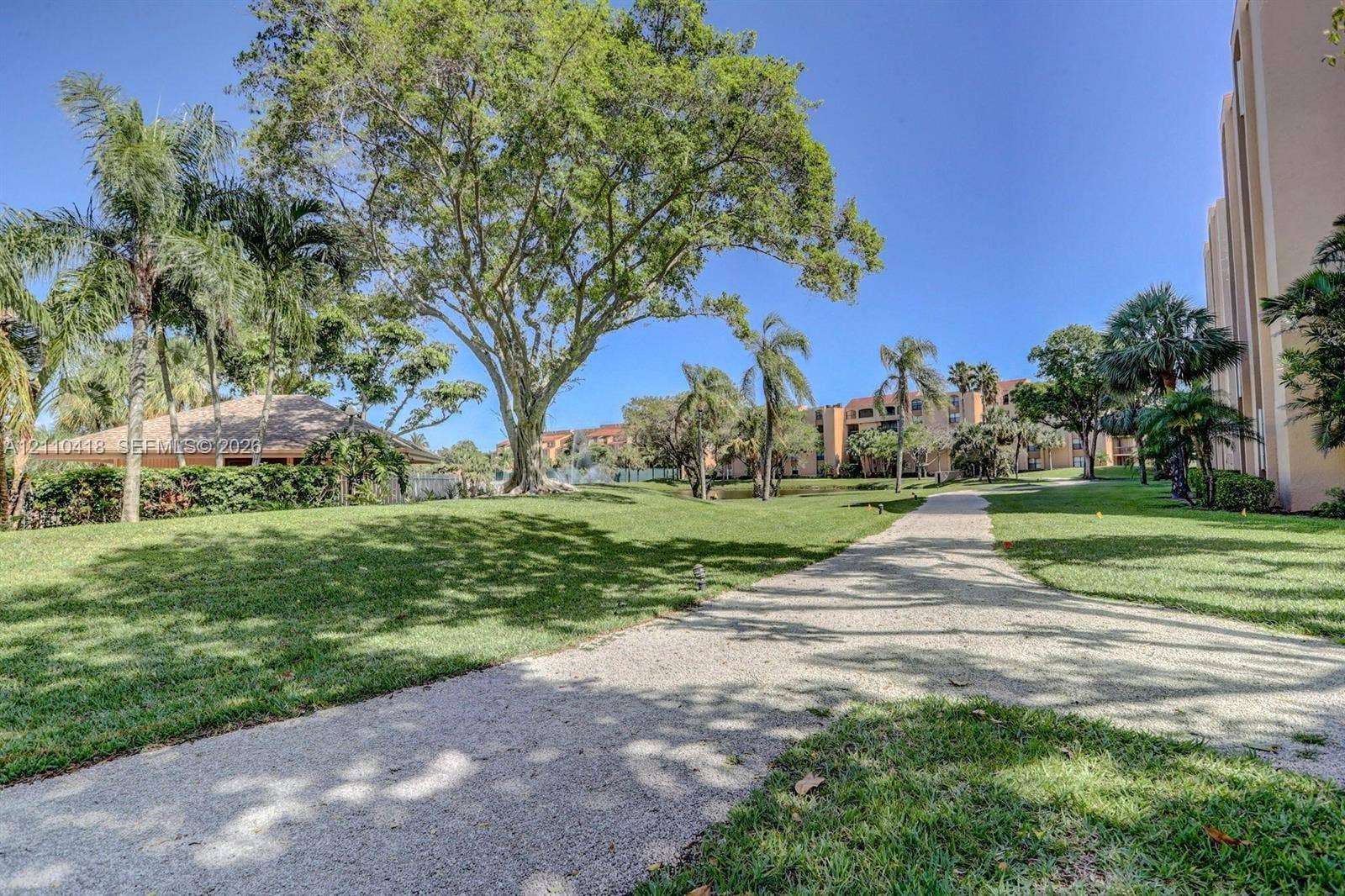 950 Egret Circle, #5409, Delray Beach, Delray Beach, FL 33444 Landscaped grounds featuring mature canopy trees, palm trees, expansive grass lawns, and a paved stone pathway