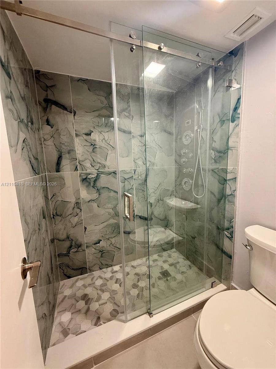 950 Egret Circle, #5409, Delray Beach, Delray Beach, FL 33444 Walk-in shower featuring large-format patterned wall tile, hexagonal floor tiling, a frameless glass sliding door, and integrated body spray jets