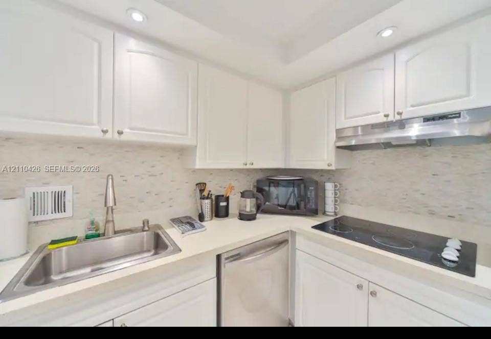 Kitchen featuring white shaker-style cabinetry, a stone-finish countertop, textured mosaic tile backsplash, stainless steel dishwasher, and a glass-top electric cooktop with a stainless steel range hood