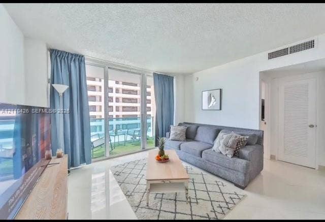 Living area featuring expansive floor-to-ceiling glass sliding doors, private balcony, neutral large-format tile flooring, and a louvered closet door