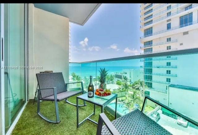 Private balcony with glass panel railing, artificial turf flooring, and floor-to-ceiling sliding glass door access