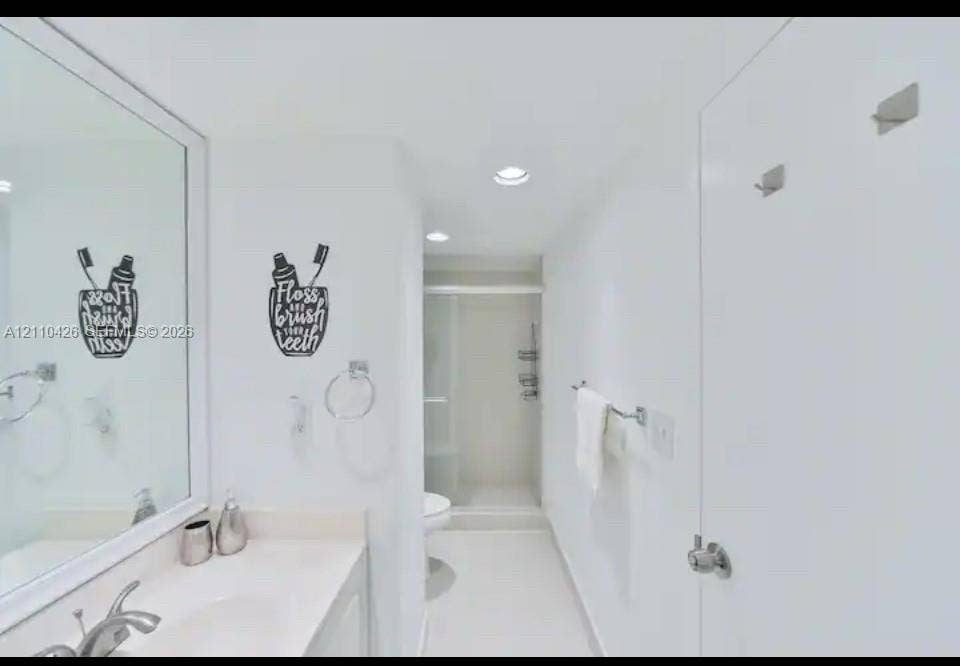 Bathroom featuring a large vanity mirror, solid-surface countertop with an integrated sink, polished chrome faucet, recessed ceiling lighting, and a walk-in shower enclosure