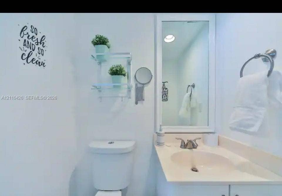 Vanity with integrated sink, metallic dual-handle faucet, framed wall-mounted mirror, and wall-mounted metal towel ring